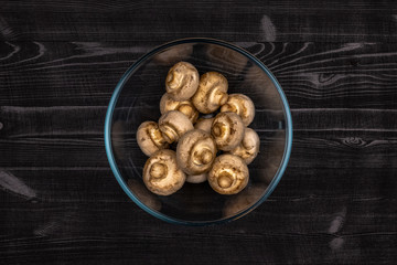 Mushrooms in a transparent glass bowl, peeled for cutting as part of the process of preparing fresh champignons for freezing