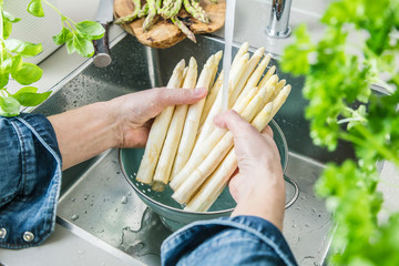 cropped shot of male hands in soil washing fresh asparagus in kitchen sink