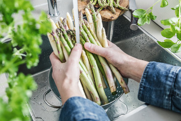 cropped shot of male hands in soil washing fresh asparagus in kitchen sink