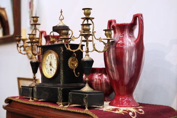 Antique clock, brass candlesticks, large vase on the shelf of the flea market