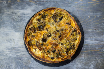  French Vegetable Quiche Lorraine pie, seen from above, on display on a rustic wooden table. It is an iconic dish of Eastern France, a pastry made of flan, cheese, milk, cream and vegetables