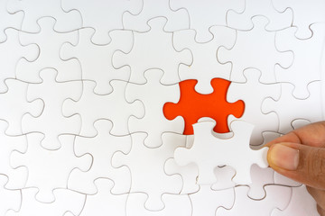 Fototapeta premium Hand put the last piece of jigsaw puzzle closeup to complete the mission. Selective focus and crop fragment
