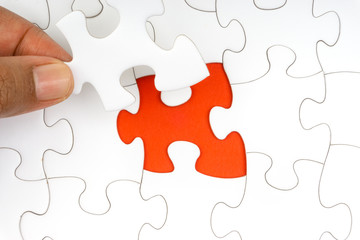 Fototapeta premium Hand put the last piece of jigsaw puzzle closeup to complete the mission. Selective focus and crop fragment