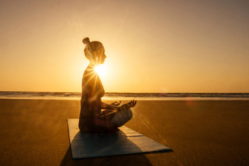Silhouette of young woman in a stylish suit for yogi jumpsuit doing yoga on the beach in pose copy...
