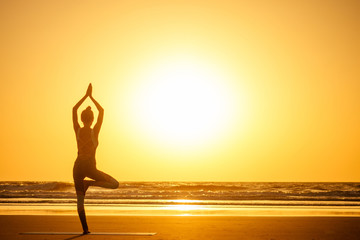 Silhouette of young woman in a stylish suit for yogi jumpsuit doing yoga on the beach in pose copy...