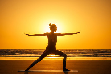 Silhouette of young woman in a stylish suit for yogi jumpsuit doing yoga on the beach in pose copy space