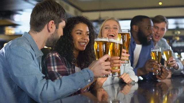 Emotional sport fans clinking beer glasses, celebrating team victory in pub