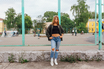 Fashion portrait of trendy young woman wearing sunglasses, and bomber jacket sitting next to rabitz in the city