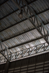 Obraz premium An interior space of a factory shop showing a scaffolding metal roof sheet with a framework of metal truss with sunlight goes through.