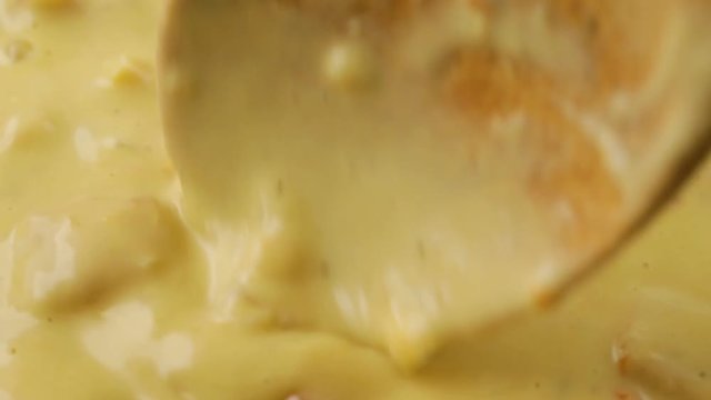 Close video of stirring hot chicken corn chowder in a pan while heating with a wood spoon illuminated with natural lighting.