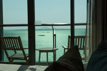 Nice sea view with clear blue sky from a balcony of a luxury hotel during a sun set scene. Seeing islands and boats as background while a rattan chair and round table in foreground.