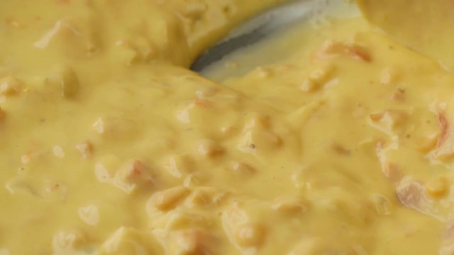 Close video of stirring cold chicken corn chowder in a pan for heating with a wood spoon illuminated with natural lighting.
