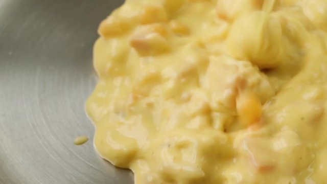 Close video of adding cold chicken corn chowder to a pan for heating illuminated with natural lighting.