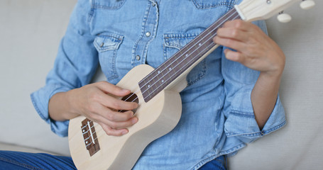 Woman sit on sofa and play with ukulele at home
