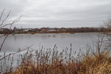 Yellow landscape in autumn cloudy day with yellow grass, a lake and a village on the other side