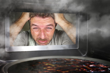 messy and funny dummy man in the kitchen looking through microwave or oven pizza burning overcooked...