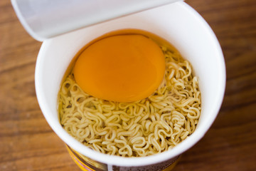 raw instant noodle in cup add egg on wood background
