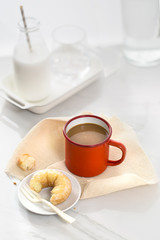 Coffee break time table top shot with a mug of coffee and sugary donut on white background.