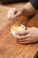 The customer mixes sugar in a hot cappuccino with a wooden disposable stick.