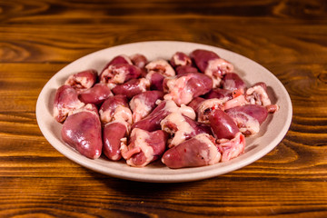 Ceramic plate with raw chicken hearts on wooden table