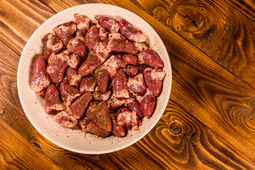 Ceramic plate with raw chicken hearts on wooden table. Top view