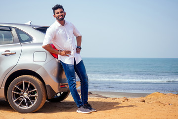 travel vacation happy indian man in white shirt collar buying new car and showing the key, sitting in car on beach sea india octan Goa .a trip to the beach in car