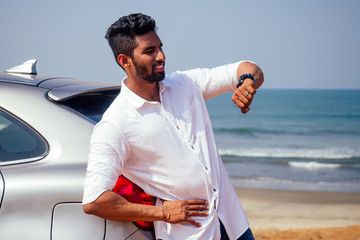 handsome and successful indian man in a stylish well-dressed freelancer working with a laptop on the beach.freelance and remote work.businessman student in a summer cafe on the shore of india ocean