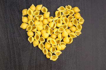 Raw macaroni - conchiglie paste shells in the shape of a heart on a dark background.