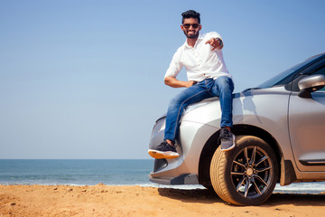 Indian businessman standing near car outdoors on sea beach summer good day.a man in a white shirt...