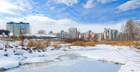 Panorama of the city with colorful new buildings on the river bank in winter.