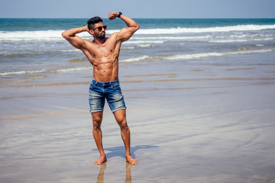 Handsome muscular dark haired surfer athletic muscular and healthy black man on beach during summer morning warm up ocean india sea Goa vacation
