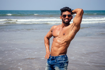 Topless athletic, muscular and healthy black man warm up instructor on the beach.indian male...