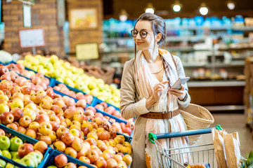 Young woman looking on the shopping list using smartphone while shopping food in the supermarket