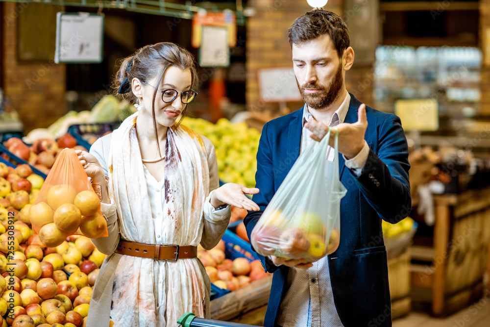 Wall mural man and woman buying food using eco and plastic bag in the supermarket. concept of the use of eco ba