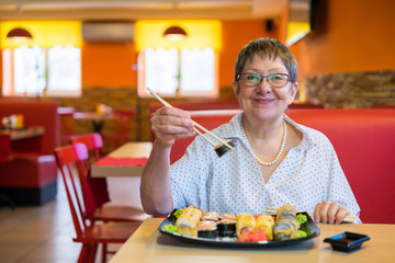 The elderly lady in the cafe restaurant is very happy and invites you to taste sushi and rolls.