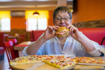Aged business woman in a cafe-restaurant is glad that she eats fast food. The problem with overweight and junk food does not interest her.