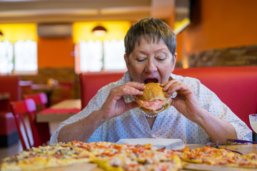 An elderly lady works a lot and decided to have a snack in a cafe restaurant. Fast food is not good for health. Overweight and fatigue.