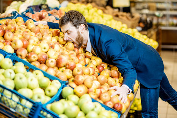 Funny portrait of a businessman hugging a pile of apples in the supermarket in the department with fruits and vegetables