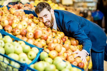 Funny portrait of a businessman hugging a pile of apples in the supermarket in the department with fruits and vegetables