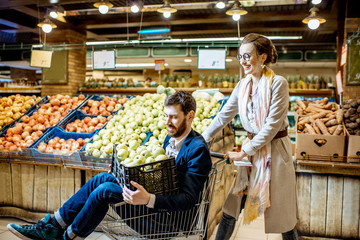 Happy couple having fun while riding in the shopping cart in the supermarket buying fresh fruits