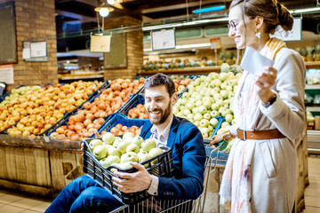 Happy couple having fun while riding in the shopping cart in the supermarket buying fresh fruits