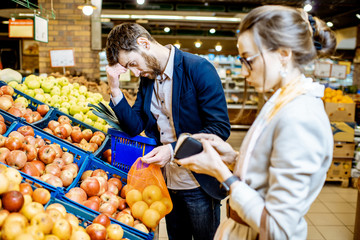 Sad couple with despired emotions having a problem with their budget buying food in the supermarket