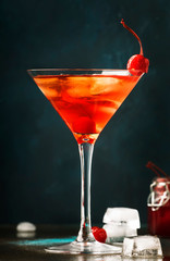 Classic alcoholic cocktail Manhattan with bourbon, red vemuth, bitter, ice and cocktail cherry in glass, gray bar counter background, place for text, selective focus
