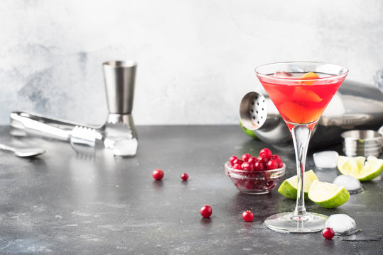 Classic alcoholic cocktail cosmopolitan with vodka, liqueur, cranberry juice, lime, ice and orange zest, gray bar counter background, bartender tols, space for text