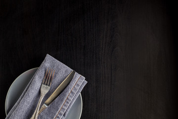 table setting with empty plate napkin fork and knife on black background