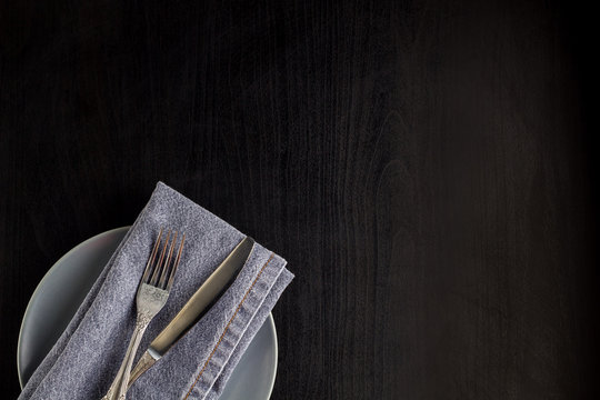 table setting with empty plate napkin fork and knife on black background