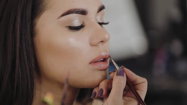 Makeup artist professionally applies lipstick on lips of a model with a beautiful face.