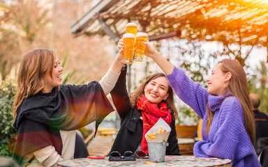 Group of women best friends clinking glasses of beer in restaurant - female friendship and having...