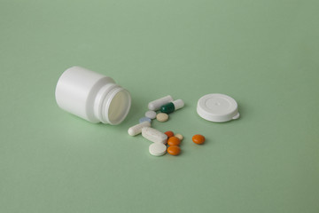 Pills, tablets and capsules and a bottle on a green background. Copy space for text.