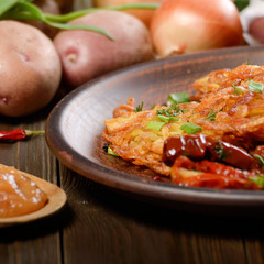 Homemade tasty potato pancakes in clay dish with applesauce